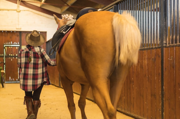 Retrato de una mujer adulta en un establo de caballos caminando un caballo marrón, vestida con trajes de América del Sur