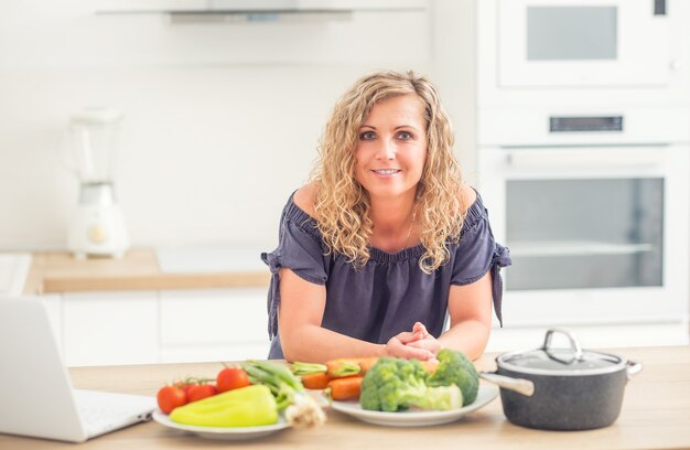 Retrato de mujer adulta feliz en su cocina moderna con olla y verduras.