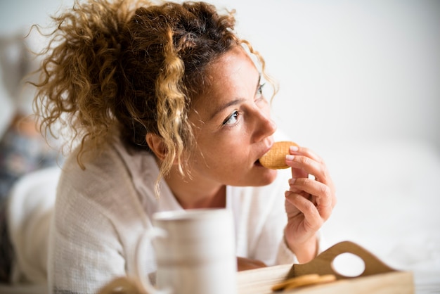 Retrato de mujer adulta hermosa comiendo galletas en el desayuno de la mañana en el dormitorio