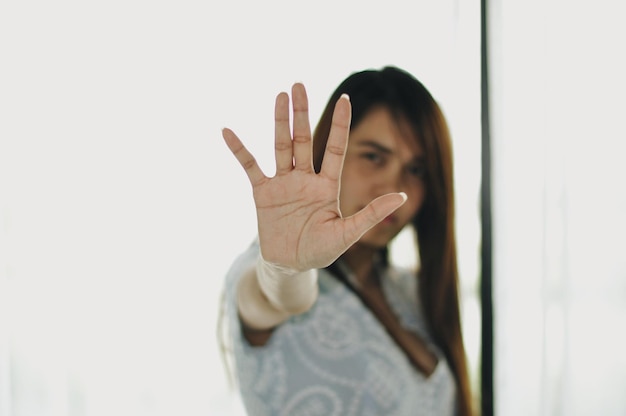 Retrato de una mujer adulta que muestra un gesto de parada mientras está de pie contra la pared