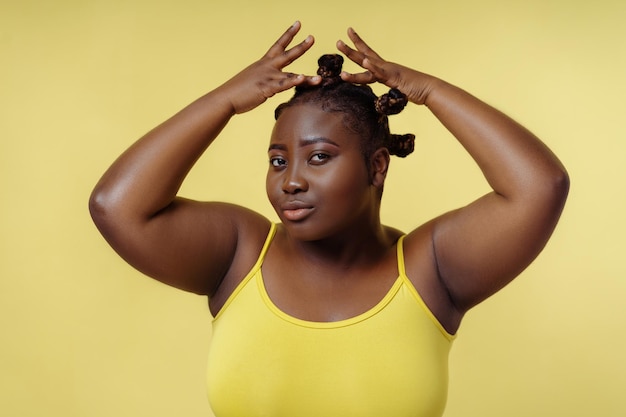 Retrato de una mujer africana hermosa y glamorosa arreglando un peinado elegante mirando a la cámara aislada en un fondo amarillo Mujer atractiva posando para la foto Concepto de belleza