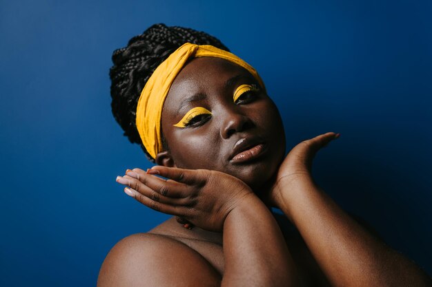 Foto retrato de una mujer africana segura de sí misma con un hermoso maquillaje y una cara conmovedora sobre un fondo azul