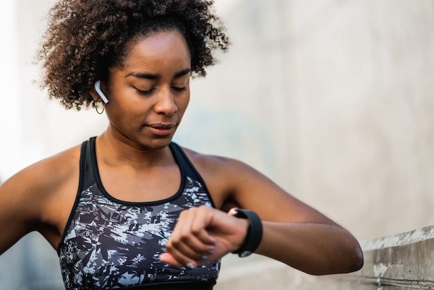 Retrato de mujer afro atleta comprobando el tiempo en su reloj inteligente. Concepto de deporte y estilo de vida saludable.