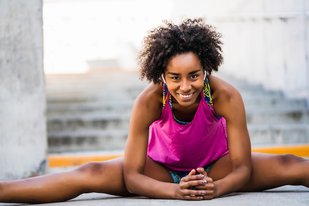 Retrato de mujer afro atleta estirando las piernas antes de hacer ejercicio al aire libre