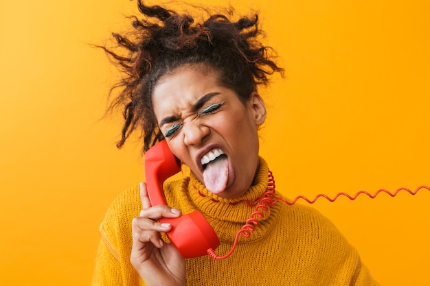 Retrato de mujer afroamericana alegre con peinado afro gritando y sosteniendo el auricular rojo, aislado
