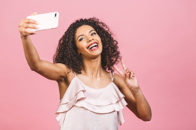 Retrato de una mujer afroamericana bastante joven en vestido mientras está de pie y tomando un selfie