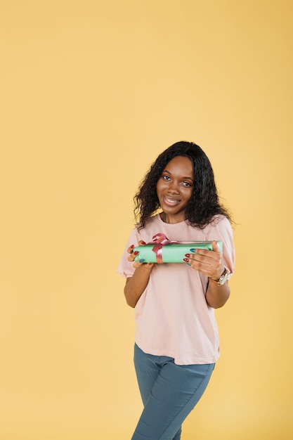 Retrato de mujer afroamericana con cabello afro con camiseta rosa posando con caja de regalo