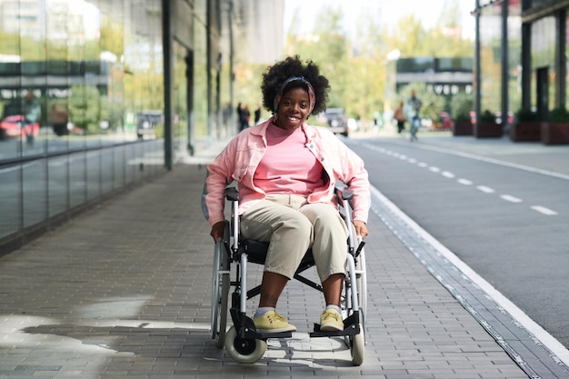 Retrato de una mujer afroamericana con discapacidad sonriendo a la cámara mientras está sentada en silla de ruedas en la ciudad