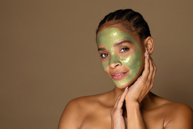 Retrato de mujer afroamericana de mediana edad con máscara verde en la cara posando sobre fondo marrón