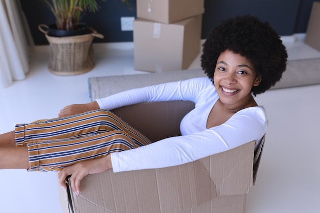 Retrato de una mujer afroamericana mudándose de casa sonriendo y sentada en una caja de cartón