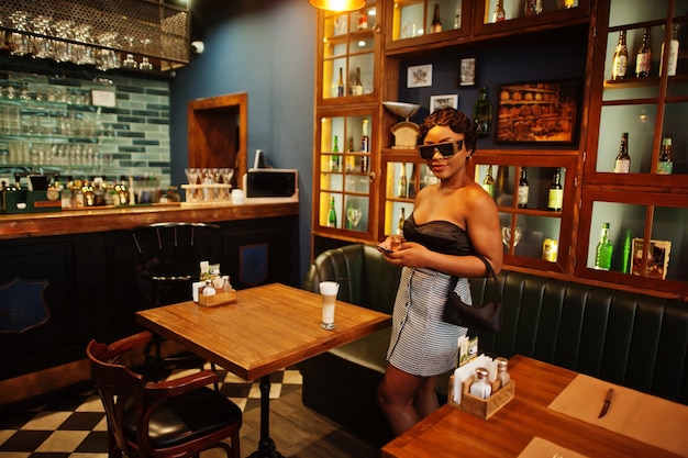 Retrato de mujer afroamericana, peinado retro posando en el restaurante con una taza de café con leche.