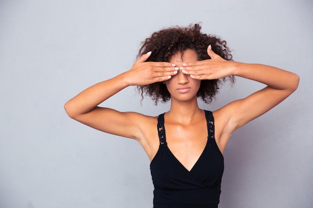 Retrato de mujer afroamericana que cubre sus ojos sobre pared gris