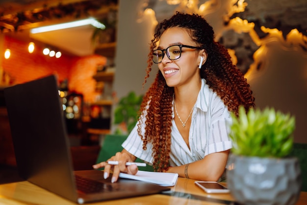 Retrato de una mujer afroamericana sentada en un café con una videollamada en una computadora portátil