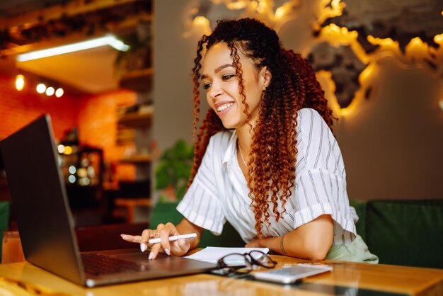 Retrato de una mujer afroamericana sentada en un café con una videollamada en una computadora portátil