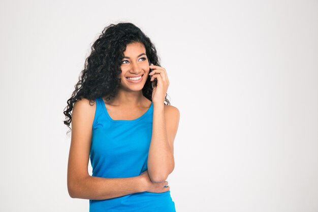 Retrato de una mujer afroamericana sonriente hablando por teléfono y mirando a otro lado aislado en una pared blanca