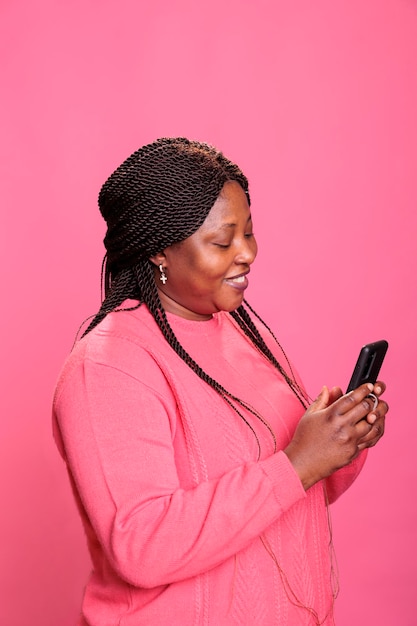 Retrato de una mujer afroamericana sosteniendo un teléfono móvil navegando en Internet, viendo videos divertidos en un teléfono inteligente relajándose durante el tiempo libre. Modelo publica foto en redes sociales