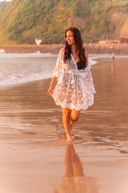 Retrato de una mujer al atardecer con un vestido blanco disfrutando de las vacaciones en la playa