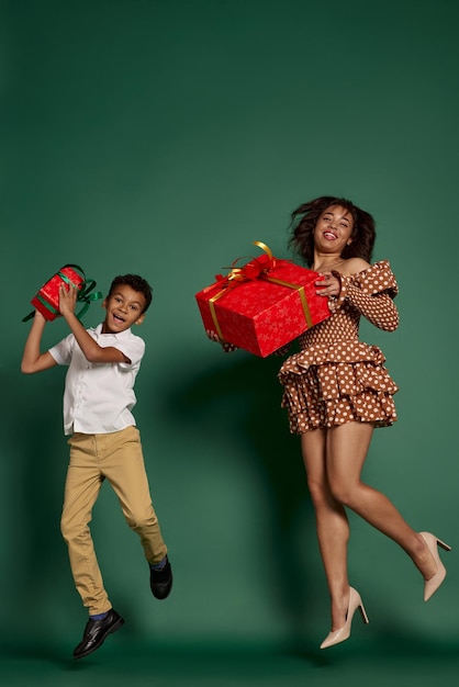 Retrato de mujer alegre y adolescente saltando de emoción con cajas presentes aisladas sobre verde