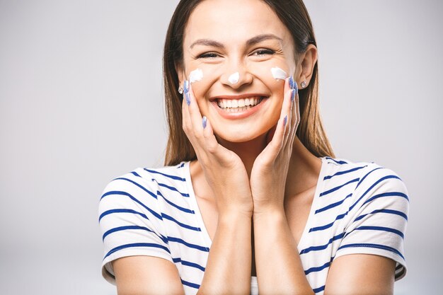 Retrato de una mujer alegre aplicando crema facial