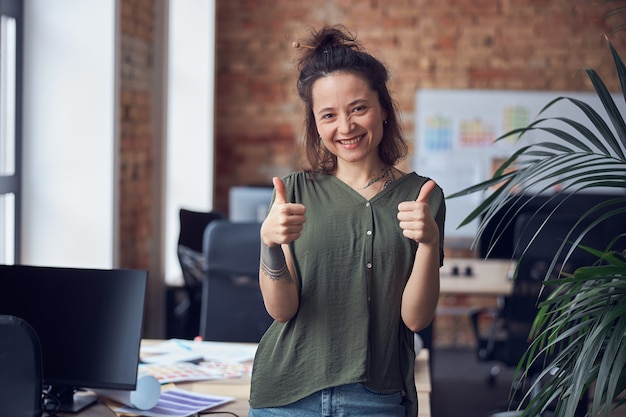 Foto retrato de mujer alegre diseñador de interiores o arquitecto sonriendo a la cámara mostrando thums mientras