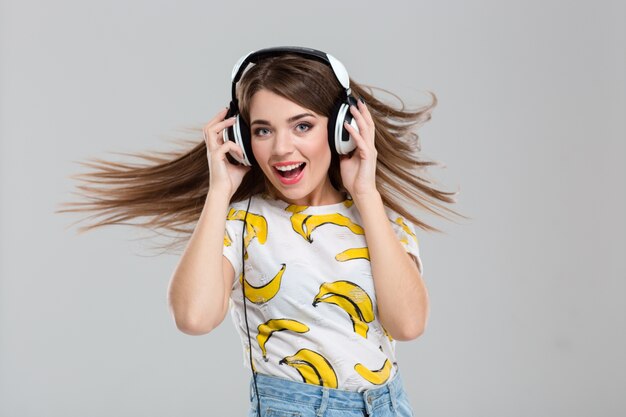 Retrato de una mujer alegre escuchando música en auriculares aislado sobre un fondo blanco.