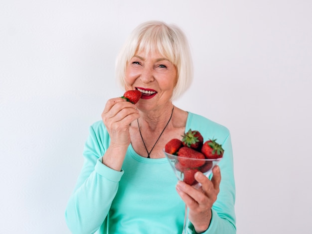 Retrato de mujer alegre con estilo antiguo senior en ropa turquesa comiendo fresas