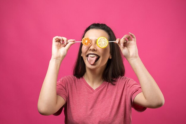 Retrato de mujer alegre hermosa dulce encantadora con cabello castaño lacio sosteniendo una piruleta cerca de los ojos.