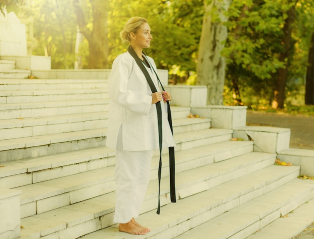 Retrato de una mujer alegre luchadora en kimonos blancos con cinturón negro al aire libre