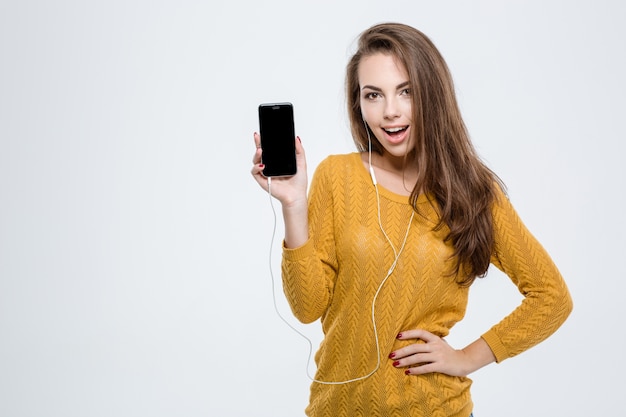 Retrato de una mujer alegre que muestra la pantalla del teléfono inteligente en blanco aislado en un fondo blanco.