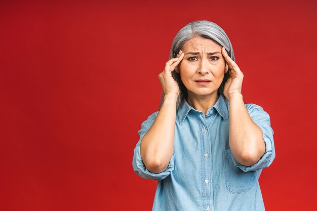 Retrato de mujer anciana madura enferma cansada estresada aislada sobre fondo rojo Concepto de dolor de cabeza