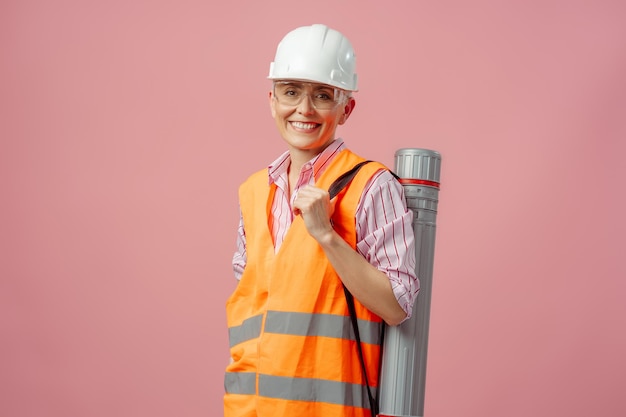 Retrato de una mujer arquitecta ingeniera con una sonrisa confiada, con un sombrero duro, mirando a la cámara de pie, con un fondo rosa aislado, un concepto de negocio exitoso