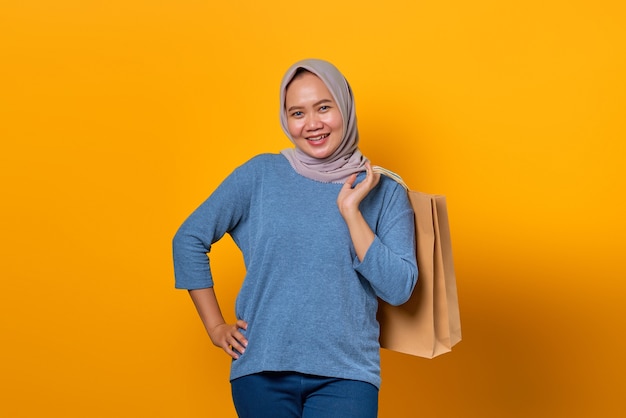 Retrato de mujer asiática alegre sosteniendo bolsa de compras sobre fondo amarillo