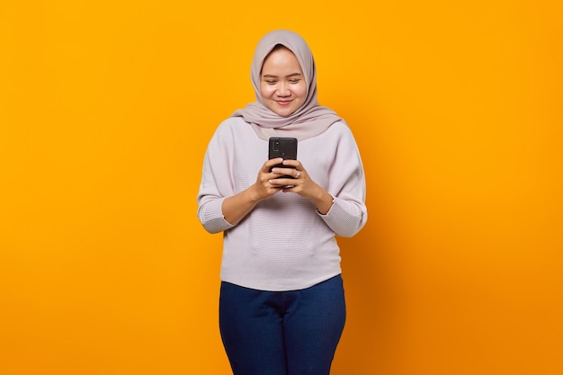 Retrato de mujer asiática atractiva alegre mediante teléfono móvil sobre fondo amarillo