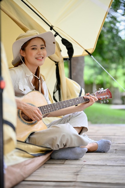 Retrato mujer asiática canta una canción mientras toca la guitarra en su tienda Camping y actividad al aire libre