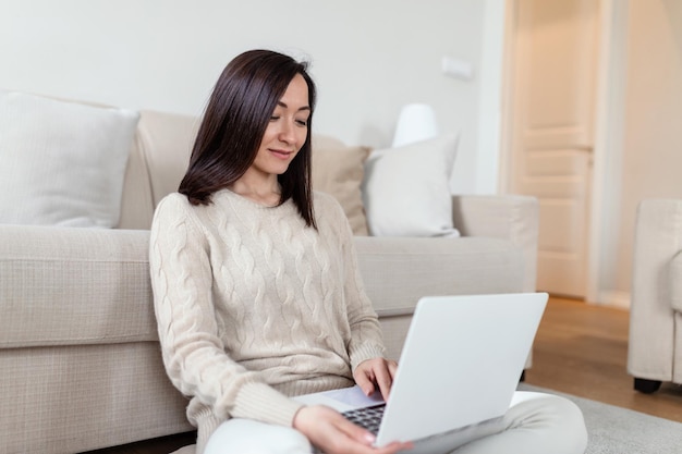Retrato de una mujer asiática casual relajada sentada en el suelo usando una computadora portátil pensando asiática propietaria de una pequeña empresa independiente con concepto de trabajo virtual desde casa