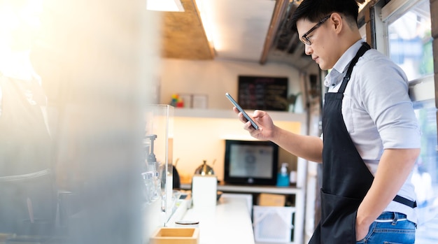 Retrato de mujer asiática confía en barista de pie dentro del autobús café cafÃƒÂ ©. El propietario de una empresa PYME utiliza un teléfono inteligente para el marketing online.