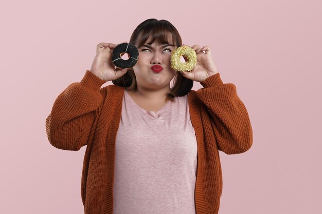 Retrato de mujer asiática y donuts. Chica mostrando donuts frente a sus ojos sobre fondo rosa.