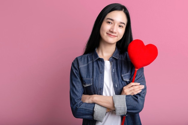 Retrato de mujer asiática encantadora abrazando corazón aislado sobre fondo rosa Símbolo de corazón rojo del día de San Valentín mujer asiática sonriente espera