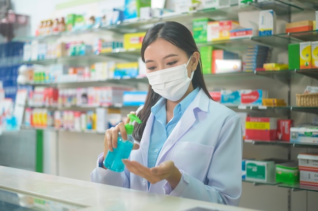 Un retrato de una mujer asiática farmacéutica con una mascarilla quirúrgica con gel de alcohol en una farmacia moderna, covid-19 y concepto de pandemia.