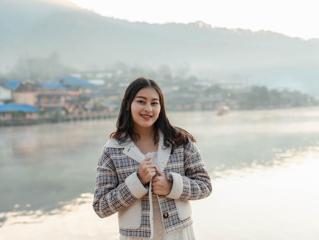 Retrato de mujer asiática feliz en chaqueta de invierno con niebla en la vista del lago por la mañana en la aldea tailandesa de Ban Rak, Mae Hong Son en Tailandia.