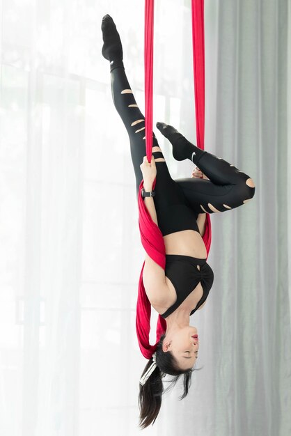 Foto retrato de una mujer asiática feliz en una clase de yoga aéreo una mujer asiática haciendo ejercicios de estiramiento de yoga con mosca