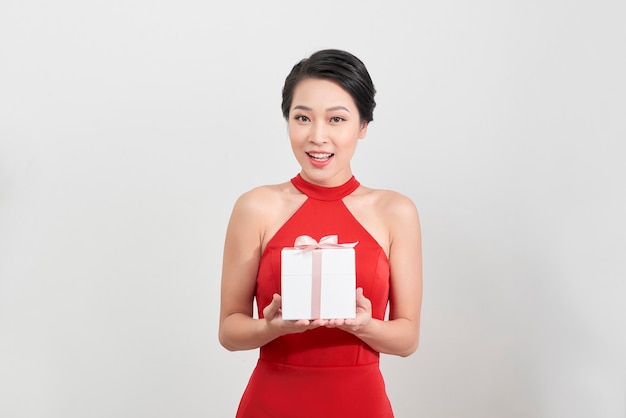 Retrato de una mujer asiática feliz mostrando caja de regalo y mirando a cámara aislada sobre fondo blanco.