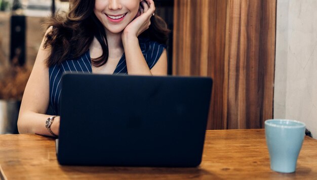 Retrato de una mujer asiática feliz y sonriente que se relaja usando la tecnología de una computadora portátil sentada en una silla