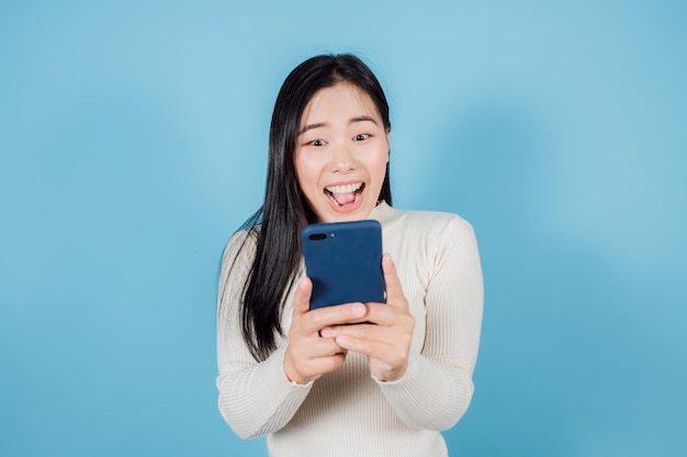 Retrato de mujer asiática feliz sosteniendo teléfono móvil o smartphone sobre fondo azul.