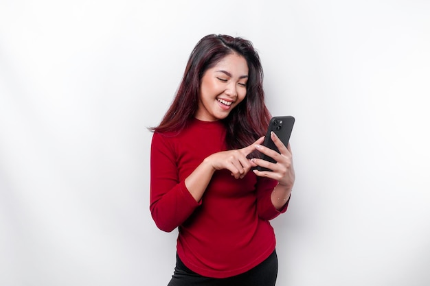 Un retrato de una mujer asiática feliz vestida de rojo y sosteniendo su teléfono aislado de fondo blanco