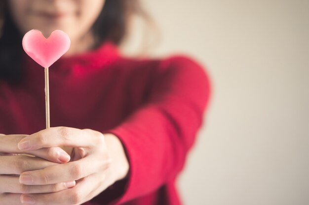 El retrato de la mujer asiática feliz se vistió en el suéter rojo que sostenía el caramelo rosado del corazón.