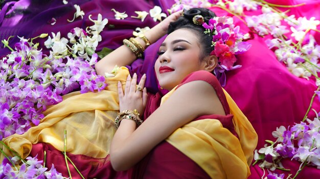 Retrato de la mujer asiática hermosa del pelo negro largo con el traje tradicional de Tailandia que miente por la flor. Concepto de viaje y estilo de vida.