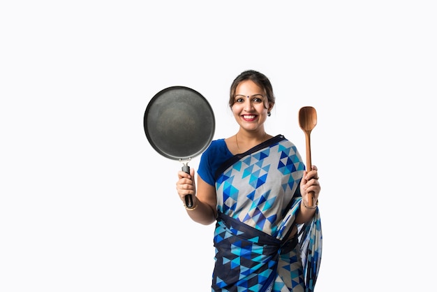 Retrato de una mujer asiática india en sari en la cocina, sosteniendo un cucharón de madera, belan, espátula o sartén, aislado contra la pared blanca