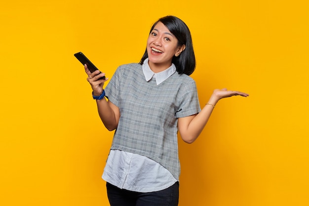 Retrato de mujer asiática joven alegre que sostiene el teléfono inteligente apuntando al espacio vacío con las palmas