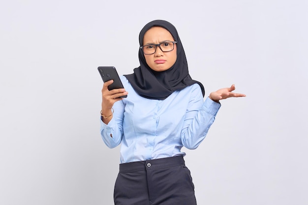 Retrato de mujer asiática joven confundida mediante teléfono móvil aislado sobre fondo blanco.